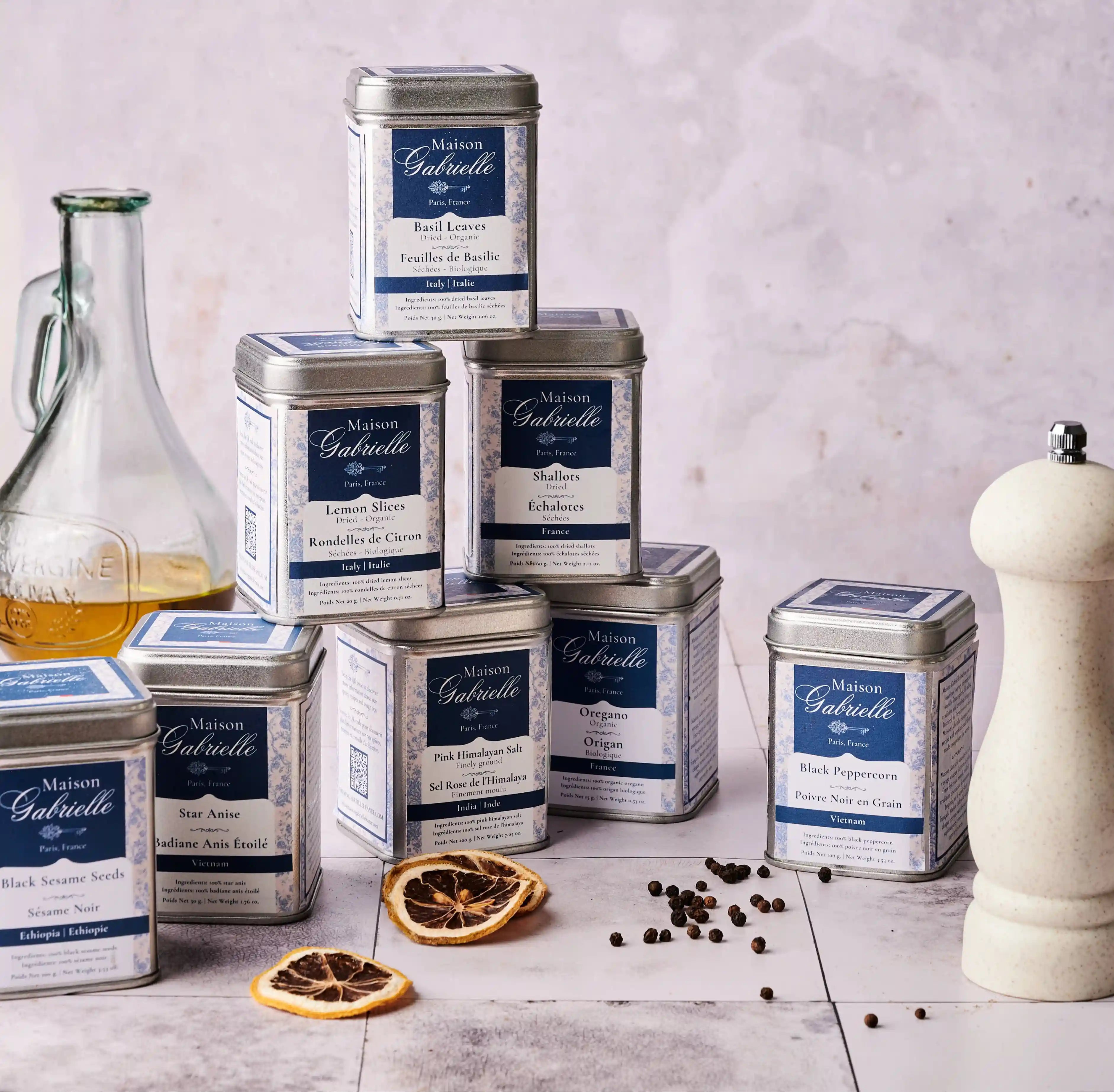Maison Gabrielle Signature Collection of Premium Spice Tins, including French Basil, Star Anise, and Pink Himalayan Salt, professionally styled with olive oil and artisanal pepper mill for the brand's official web cover.
